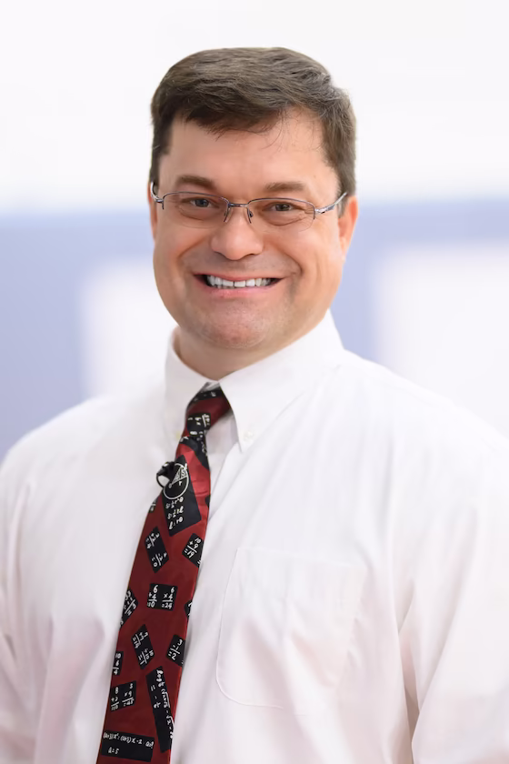 Brown-haired white man wearing white shirt, red tie, and thin-framed eyeglasses